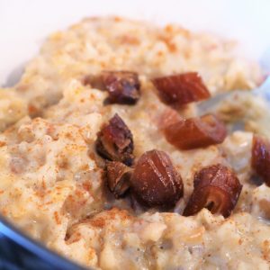 A bowl of oatmeal with raisins on top.