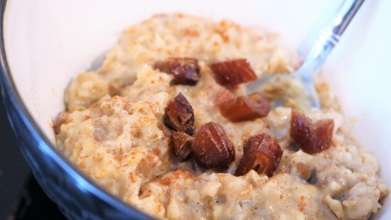 A bowl of oatmeal with raisins on top.