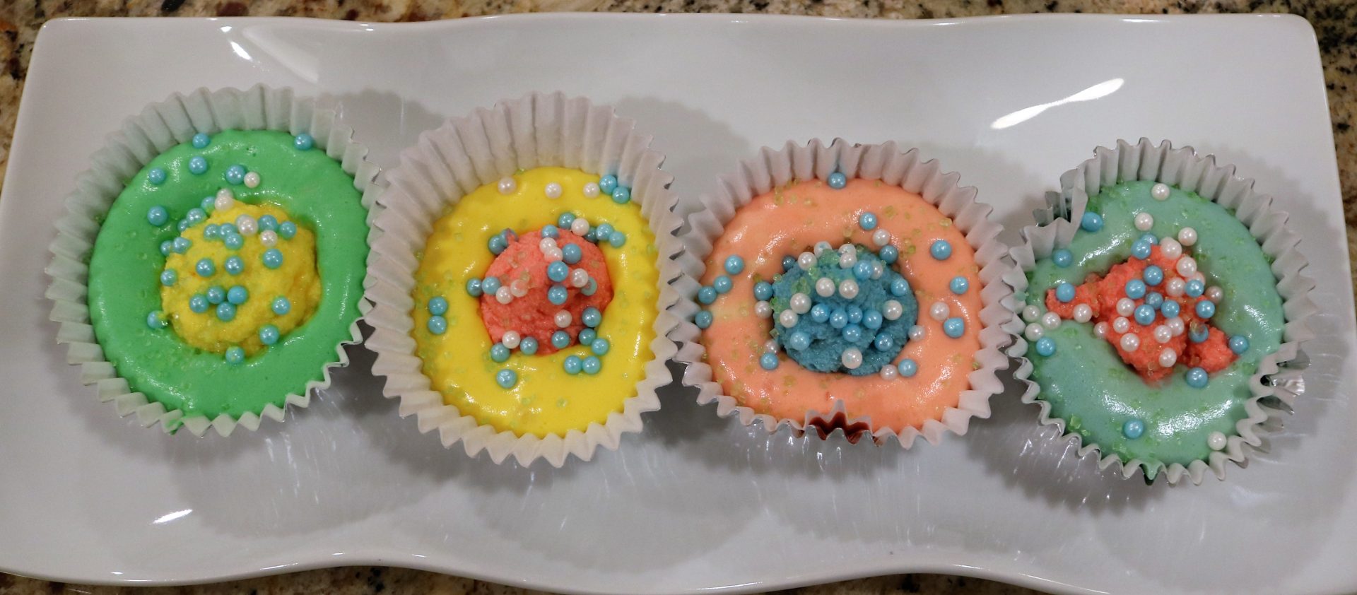 Two cupcakes with different colored frosting and sprinkles.