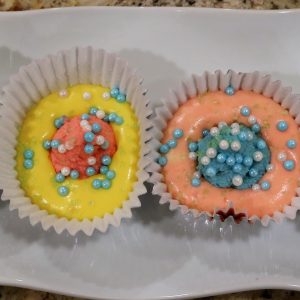 Two cupcakes with different colored frosting and sprinkles.