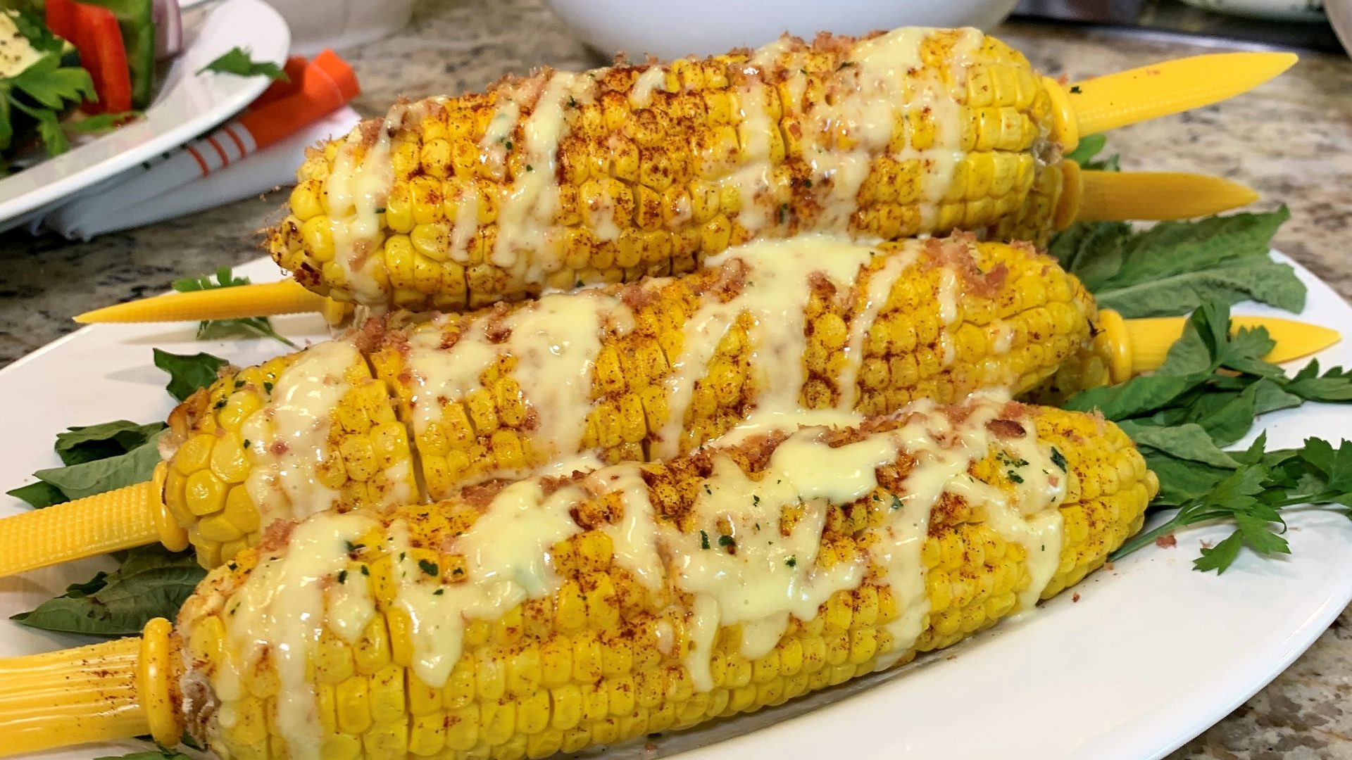 Three corn on the cob with cheese and sauce.