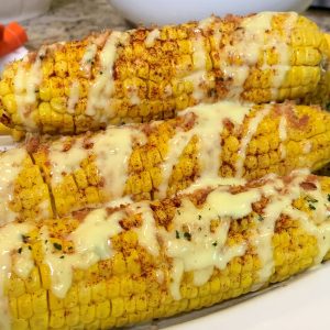 Three corn on the cob with cheese and sauce.