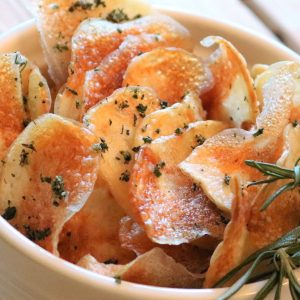 A bowl of potato chips with herbs in it.