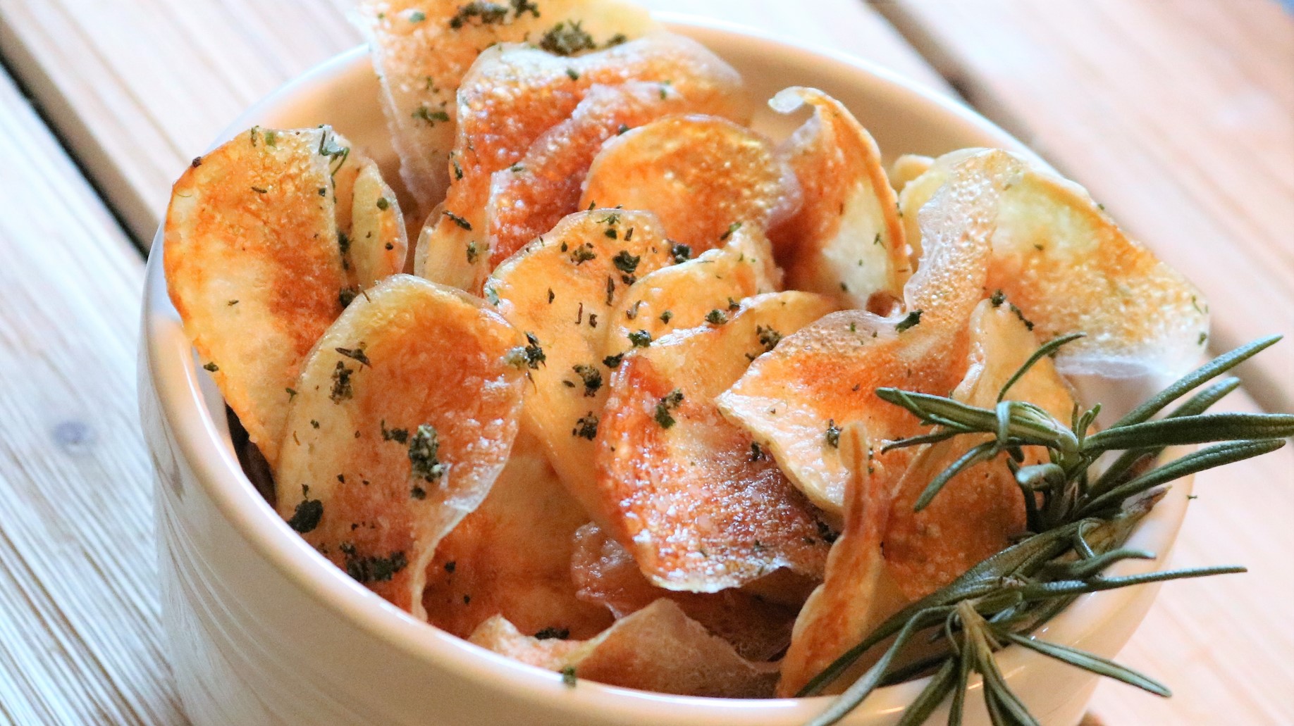 A bowl of potato chips with herbs in it.