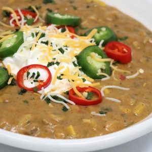 A bowl of chili with jalapenos, cheese and sour cream.