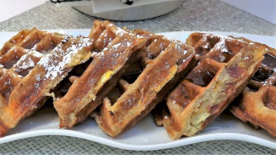 A plate of waffles covered in syrup on top of a table.
