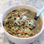 A bowl of soup with vegetables and cheese.