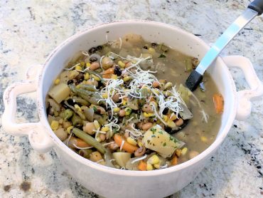A bowl of soup with vegetables and cheese.