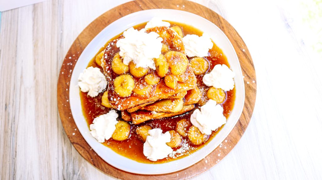 A plate of bananas and whipped cream on top of french toast.