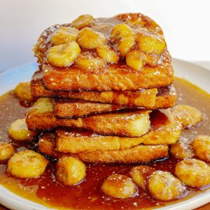 A plate of french toast covered in syrup and bananas.