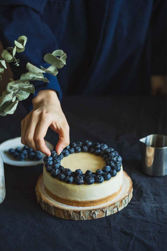 A person is decorating a cake with blueberries.