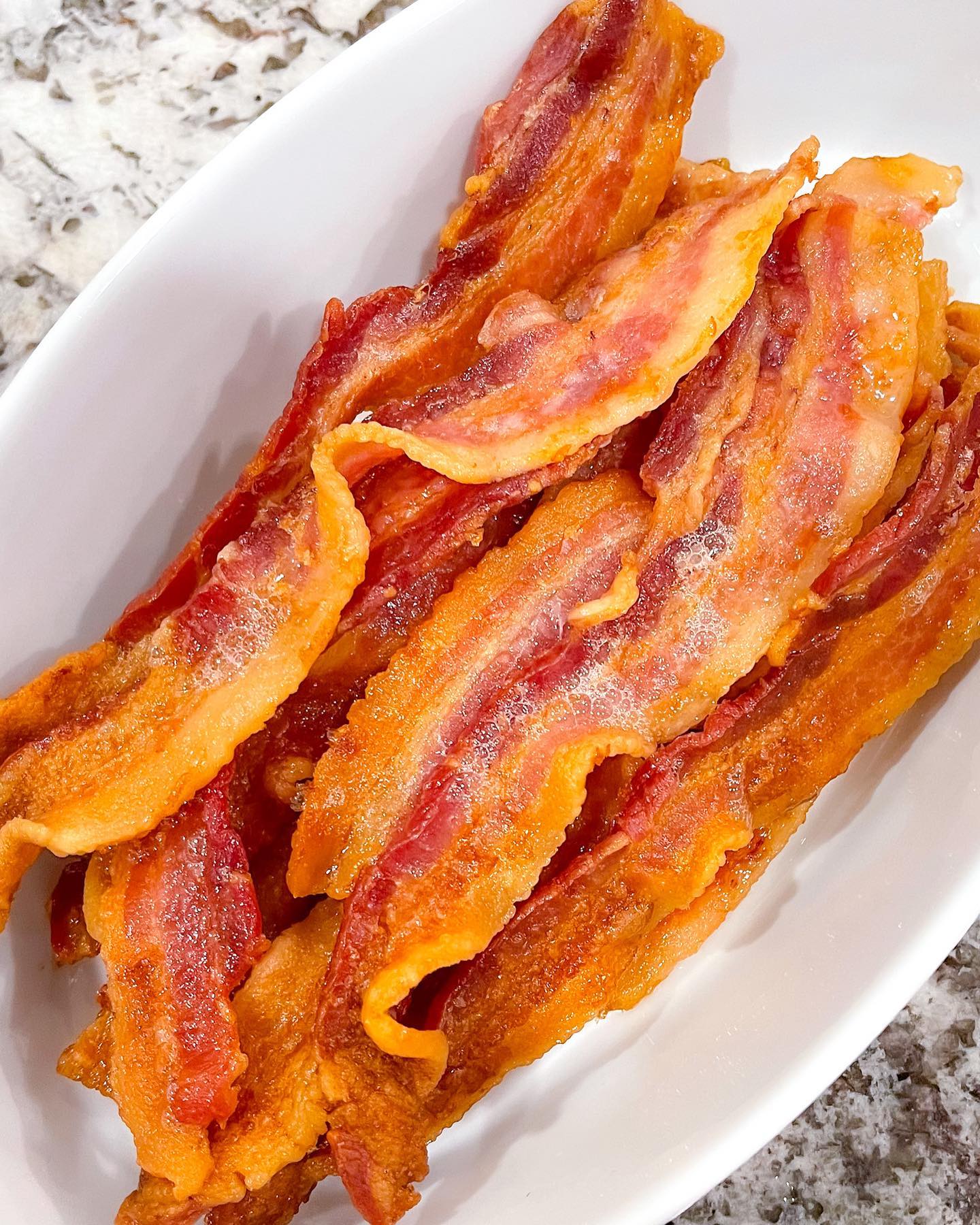 A white bowl filled with bacon strips on top of a table.